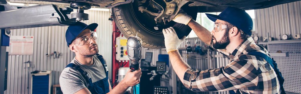 2 male GMC Maintenance professionals are servicing a tire as the vehicle is on the lift