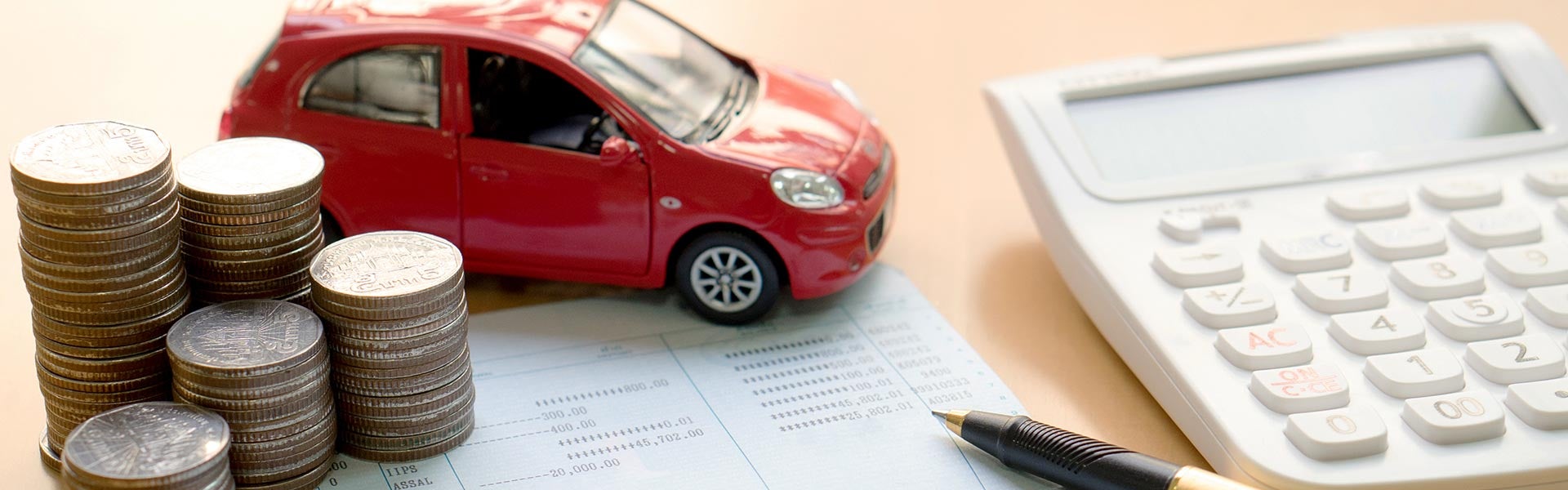 A red toy car, stacks of coins and a pen are sitting on financial agreement paperwork beside a calculator.